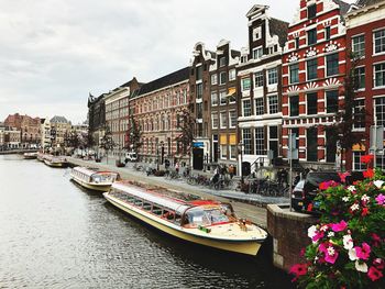 Boats moored in canal by buildings against sky in city