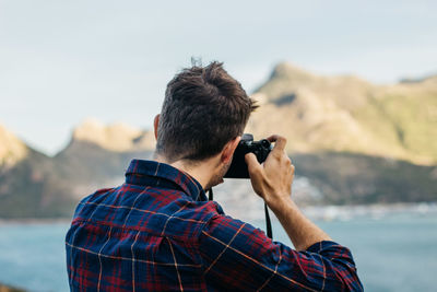 Rear view of man photographing against mountain