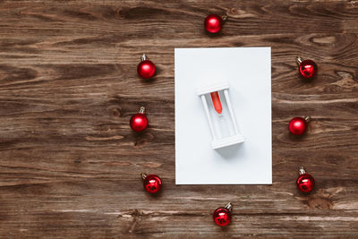 Hourglass on a blank sheet of paper and and red christmas balls on a wooden background. 