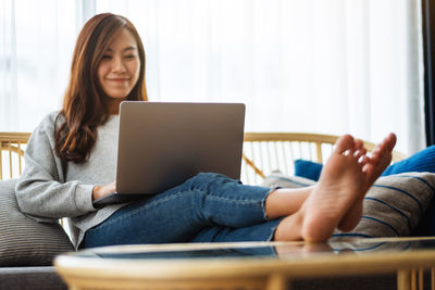 Young woman using laptop while sitting on sofa at home