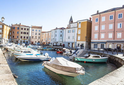 Boats moored at harbor by buildings against sky