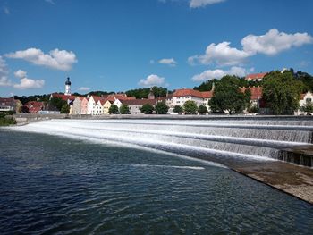 Scenic view of lake by buildings against blue sky