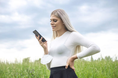 Young woman using phone while standing on field