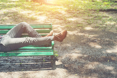 Low section of man relaxing on bench during sunny day