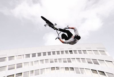 Low angle view of man doing stunt with bicycle by building against sky