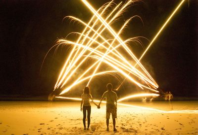 Rear view of man and woman watching light painting on beach at night