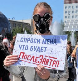 Woman wearing gas mask while holding text on paper against sky