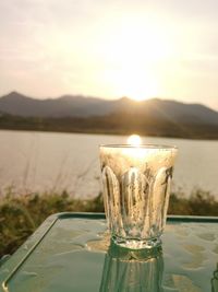 Drinking glass on lake against mountain during sunset