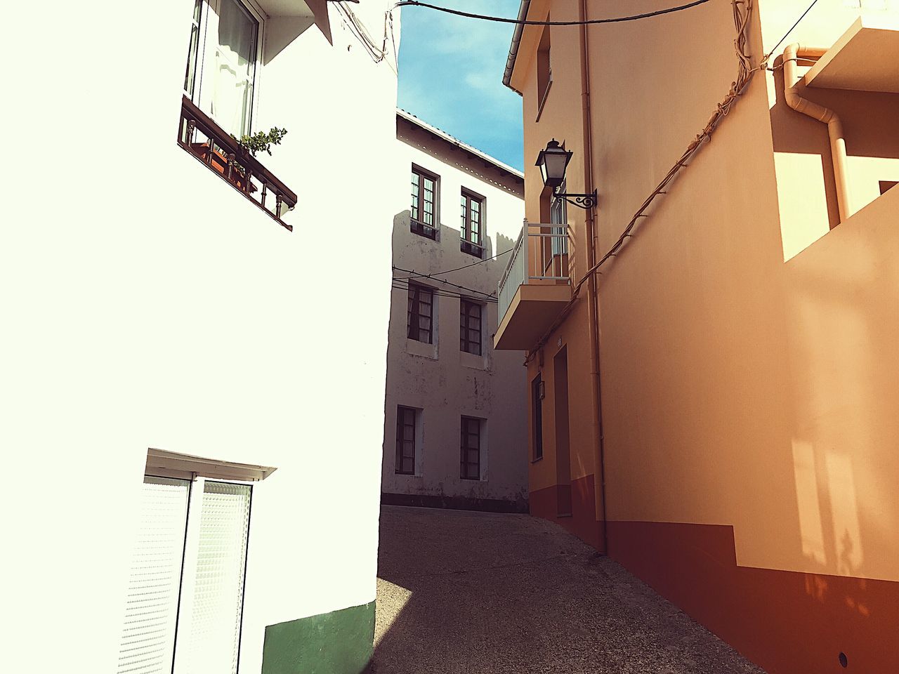 architecture, building exterior, built structure, building, residential district, no people, window, nature, sunlight, sky, day, city, lighting equipment, house, low angle view, outdoors, street, clear sky, direction, the way forward, alley, electric lamp