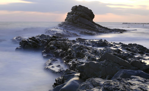 Scenic view of rocky beach against sky during sunset