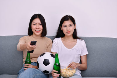 Happy friends watching sports while sitting on sofa against wall