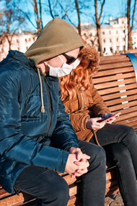 Siblings using mobile phone while sitting on bench