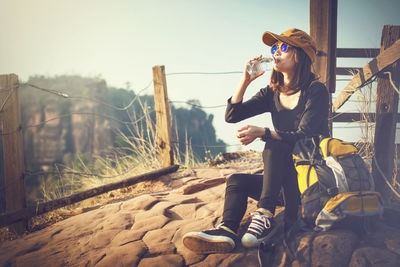Full length of hiker drinking water from bottle while sitting on rock