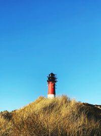 Lighthouse on field against clear blue sky