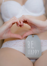 Midsection of sensuous woman making heart shape with hands by be happy tag