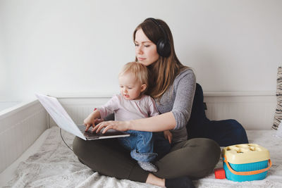 Happy woman carrying son on lap while working on laptop at home