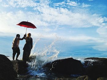 Young couple with umbrella standing on rocks at beach