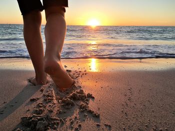 Low section of person walking at beach during sunset