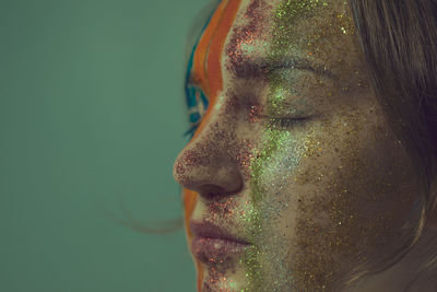 Close-up woman with painted face and closed eyes against green background