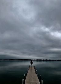 Pier over lake against cloudy sky