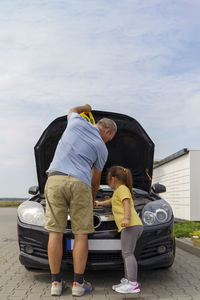 Girl helping mature man repairing car at parking lot