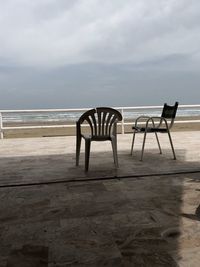 Empty chairs and table at beach against sky