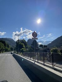 Road sign by trees against blue sky