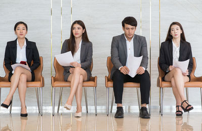 Full length of candidates holding papers while sitting on chairs in office