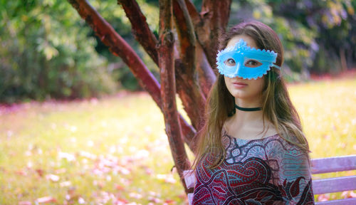 Portrait of young woman wearing venetian mask against trees