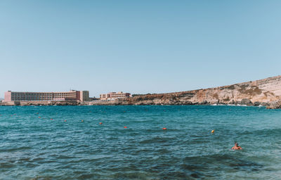 Buildings by sea against clear blue sky