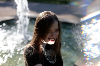 Close-up of smiling young woman against fountain