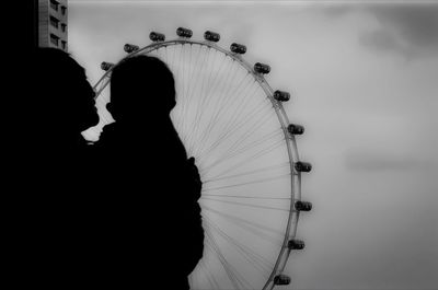 Mother with baby looking at ferris wheel against sky