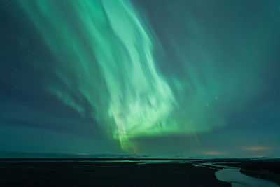 Spectacular scenery of green northern lights illuminating dark sky over snowy mountain in winter