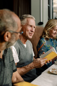 Senior man holding book while talking with male and female friends in cafe