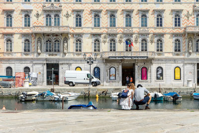 People sitting on building by canal in city