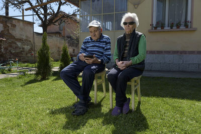 Full length of senior couple sitting at backyard against house