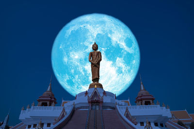 Low angle view of statue against blue sky and buildings