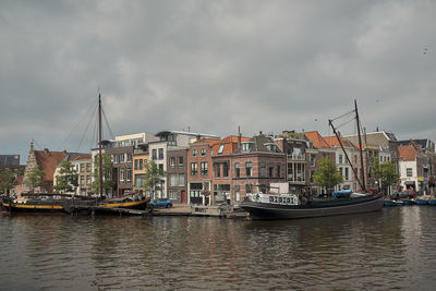 Sailboats moored on river by buildings against sky