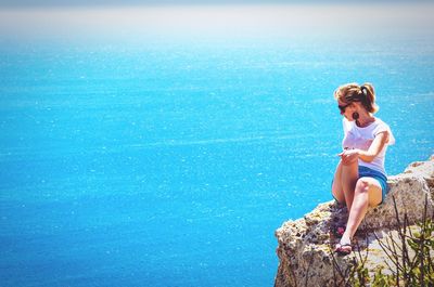 Girl sitting on rock by sea