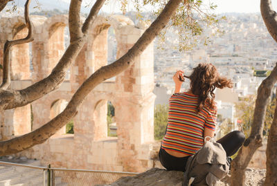 Rear view of woman sitting on branch at acropolis of athens