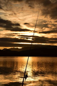 Silhouette fishing rod on sea against sky during sunset