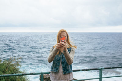 Young woman on promenade photographing with smart phone