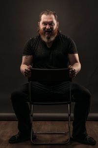Portrait of man sitting on seat against black background