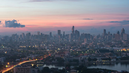 Illuminated buildings in city against sky at sunset