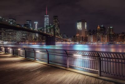 Low angle view of brooklyn bridge over river against buildings at night in city