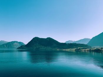 Scenic view of lake and mountains against clear blue sky