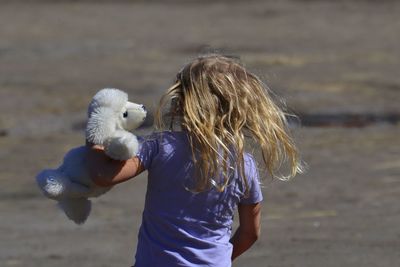 Rear view of girl with toy walking on footpath