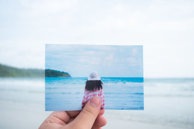 Person holding umbrella by sea against sky