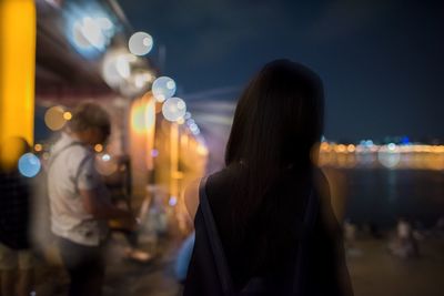 Rear view of woman standing in illuminated city at night