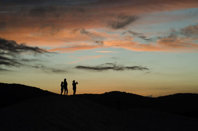Silhouette couple standing on landscape against sky during sunset